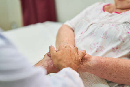 Elderly nurse or nursing service holding hands to comfort seniors in hospice or nursing home
