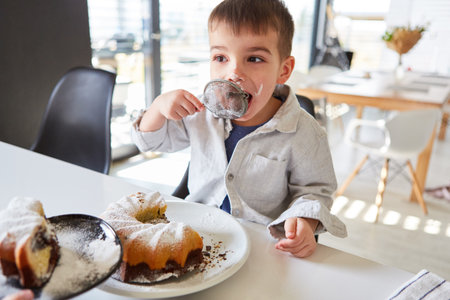 Boy nibbles powdered sugar from the sieve while baking a cake in the kitchenの写真素材
