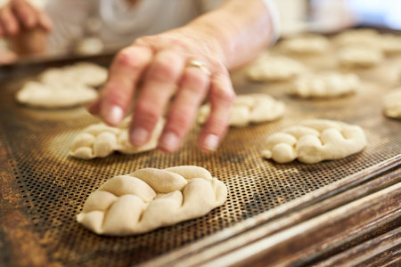 Baker's hand baking yeast plaited bread on a tray in the bakery