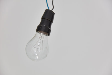 Old E27 light bulb with filament hanging in front of a white ; ; wall