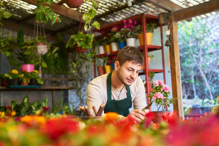 Young man as florist taking care of plants and quality control in nursery