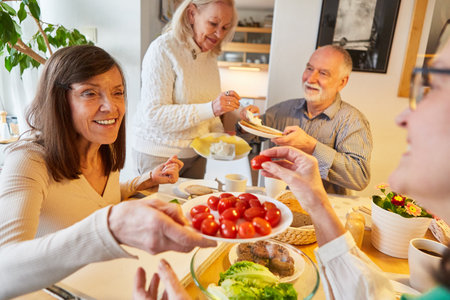 Happy group of seniors as friends eat dinner together at homeの写真素材