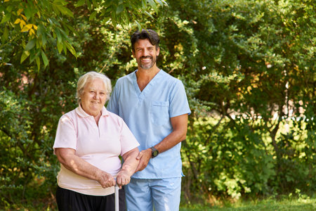 Nurse helps elderly woman with a crutch after a stroke learn to walk in the garden of the clinic