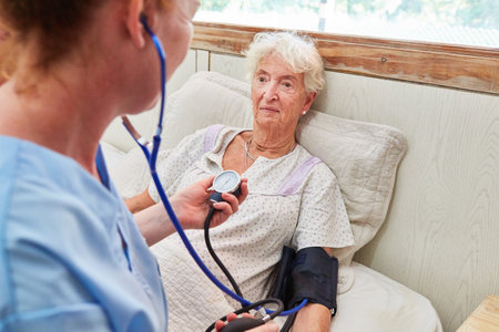 Nurse taking blood pressure of a bedridden elderly woman in bed in nursing home