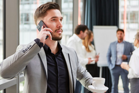 Young start-up founder talking on smartphone in office with team in backgroundの写真素材