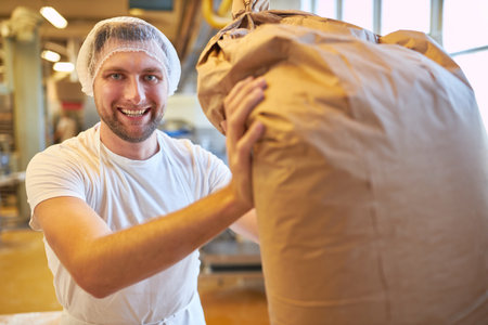 Young man as a baker apprentice or miller with a big sack of flour for the bakeryの写真素材