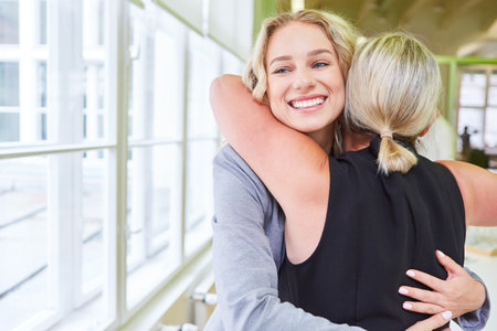 Two business women as friends hug when they meet again in the officeの写真素材