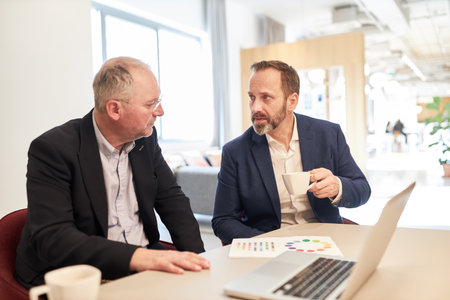 Two business people as colleagues having a casual conversation at the desk in the office