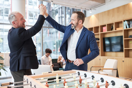 Business people play foosball at the foosball table in the office and give each other a high five