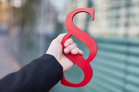 Female hand holding big red paragraph sign as law concept in front of an office building