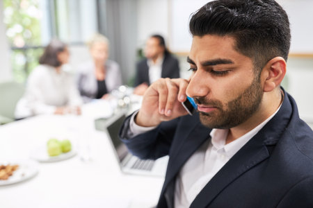 Business man talking on smartphone in meeting in office with team in backgroundの写真素材