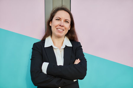 Happy smiling businesswoman with arms crossed leaning on colorful wallの写真素材