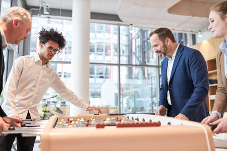 Business people playing table football at the foosball table to relax in the office lounge