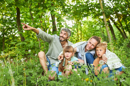 Happy father pointing while sitting with family in green forest during summer vacationの写真素材