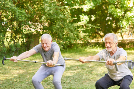 Two seniors with crutches do squats in the garden as fitness training in the retirement homeの写真素材