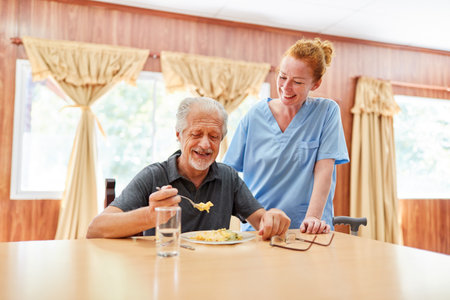 Geriatric nurse attends to senior man having lunch in nursing home or assisted livingの写真素材
