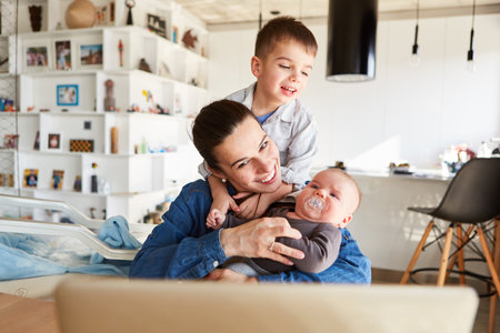 Happy mother with baby and toddler at computer streaming video in living roomの写真素材
