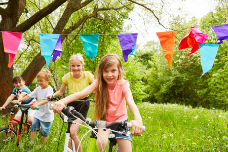 Multiracial female and male friends riding bicycles in meadow at park during summer vacationの写真素材