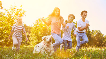 Happy family with two children and dog running around in the garden in summerの写真素材