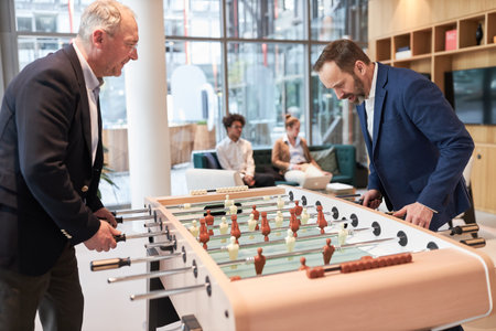 Two business people as colleagues play table football at the foosball table during a break in the...
