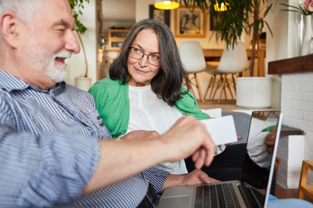 Couple of seniors with credit card shopping online on laptop computer at home as best agersの写真素材
