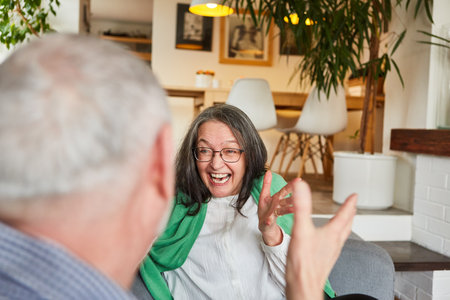 Happy senior pensioner couple laughing and rejoicing together at home in the living roomの写真素材