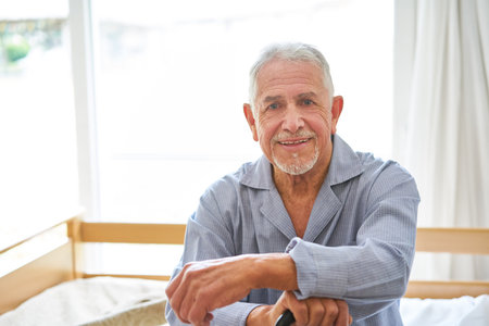 Portrait of smiling senior man wearing sleepwear sitting on bed at retirement homeの写真素材