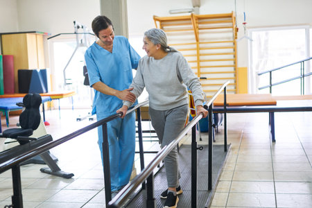 Male physiotherapist assisting happy elderly woman in movement therapy at rehab center