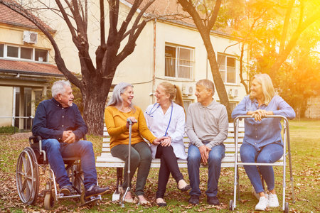 Group of five senior people sitting with doctor or nurse in garden or nursing home in summerの写真素材