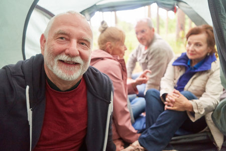 Portrait of smiling senior man with male and female friends in background inside camping tentの写真素材