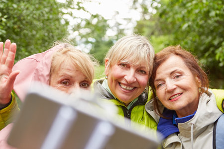 Happy senior female friends taking selfie with smartphone in forest during vacationの写真素材