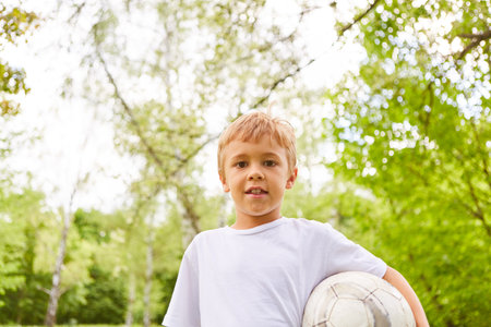 Portrait of smiling boy carrying soccer ball while standing in parkの写真素材