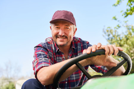 Portrait of smiling mature male farmer driving tractor with clear sky in backgroundの写真素材