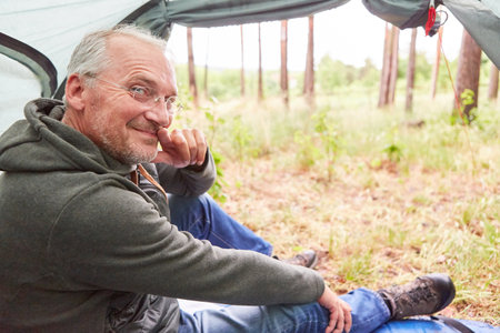Portrait of smiling senior man spending leisure time sitting in tent during campingの写真素材