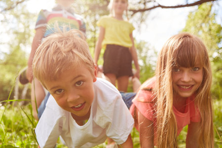 Portrait of happy children competing each other during wheelbarrow race in park on sunny dayの写真素材