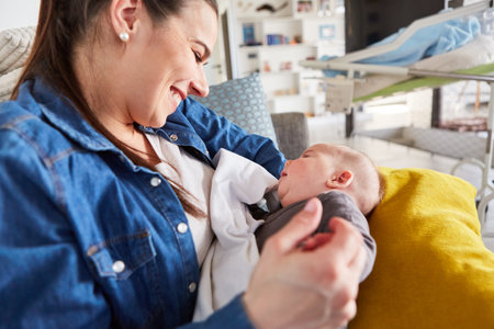 Happy mother sitting on sofa with baby in her arms after breastfeeding at homeの写真素材