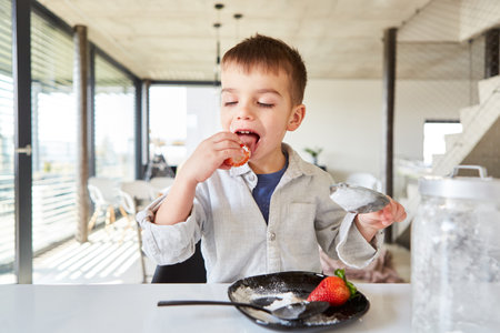 Little boy as a sweet tooth nibbles fresh strawberries with a lot of powdered sugarの写真素材