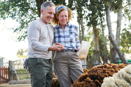 Happy male and female ranchers feeding sheep while standing in ranchの写真素材