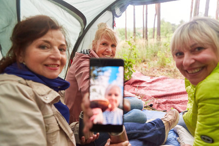 Portrait of smiling senior man showing video call on smart phone by female friends in tentの写真素材