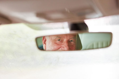 Reflection of elderly man on car's rear-view mirror during road trip