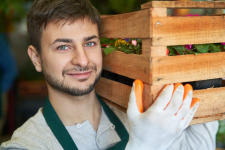 Young man as a gardener carries box of flowers on his shoulder for a delivery or orderの写真素材