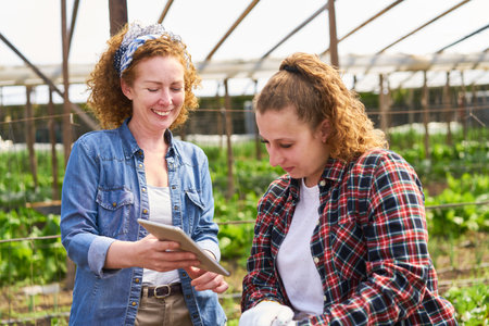 Happy female farmer sharing tablet PC with coworker at farmの写真素材