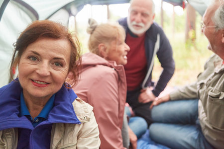Portrait of smiling senior woman with male and female friends in background inside camping tentの写真素材