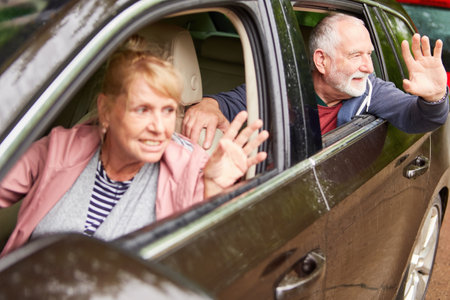 Cheerful senior couple waving hands through windows while driving car during vacationの写真素材