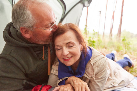 Elderly man kissing woman on head in tent during camping at forestの写真素材