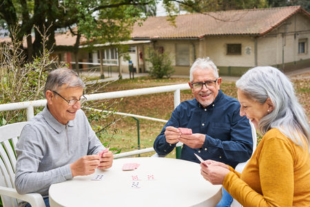 Happy senior friends playing cards on table in garden of nursing homeの写真素材
