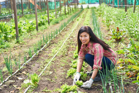 Portrait of smiling female farmer crouching amidst plants at greenhouseの写真素材