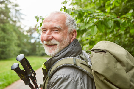 Portrait of happy senior man with hiking poles and backpack during vacationの写真素材