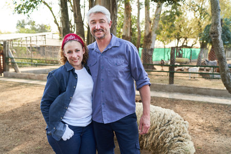 Portrait of happy female and male farmers standing with sheep at farmの写真素材