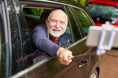 Portrait of happy senior man taking selfie with smartphone while traveling in car during vacation